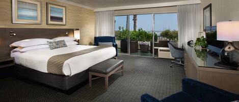 A hotel room with a large bed, a desk with a computer, a chair, and a balcony with a view.