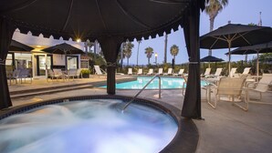 A hot tub area with lounge chairs and umbrellas, a pool, and palm trees in the background. - West Beach Inn, a Coast Hotel (Santa Barbara)