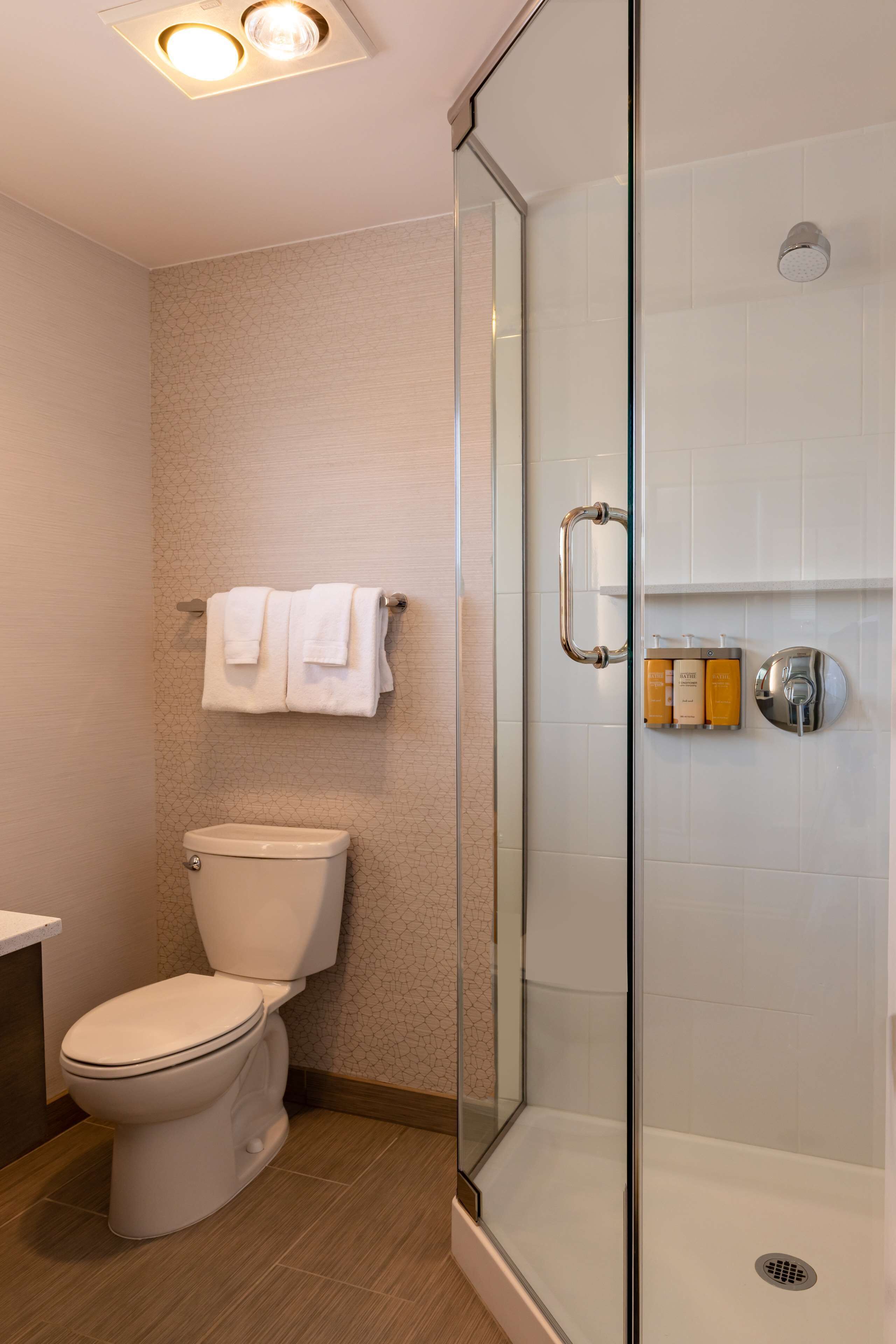 A modern bathroom with a glass-enclosed shower, a toilet, and a towel rack with folded towels.