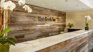A reception desk with a wooden wall and a sign that reads "West Beach Inn". - West Beach Inn, a Coast Hotel (Santa Barbara)