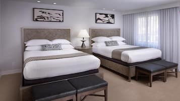 A hotel room with two beds, a bench, a nightstand, and a lamp.