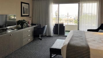 Une chambre d’hôtel équipée d’un lit, d’un bureau, d’une chaise, d’une télévision et offrant une vue sur la ville grâce à de grandes fenêtres.
