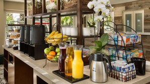 A breakfast bar with various food items, beverages, and a coffee machine. - West Beach Inn, a Coast Hotel (Santa Barbara)