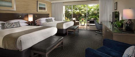 A hotel room with two beds, a desk, a chair, and a view of the outdoors.