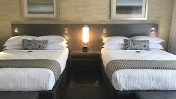 A hotel room with two beds, each with a headboard, a bedside table, and a wall-mounted light.