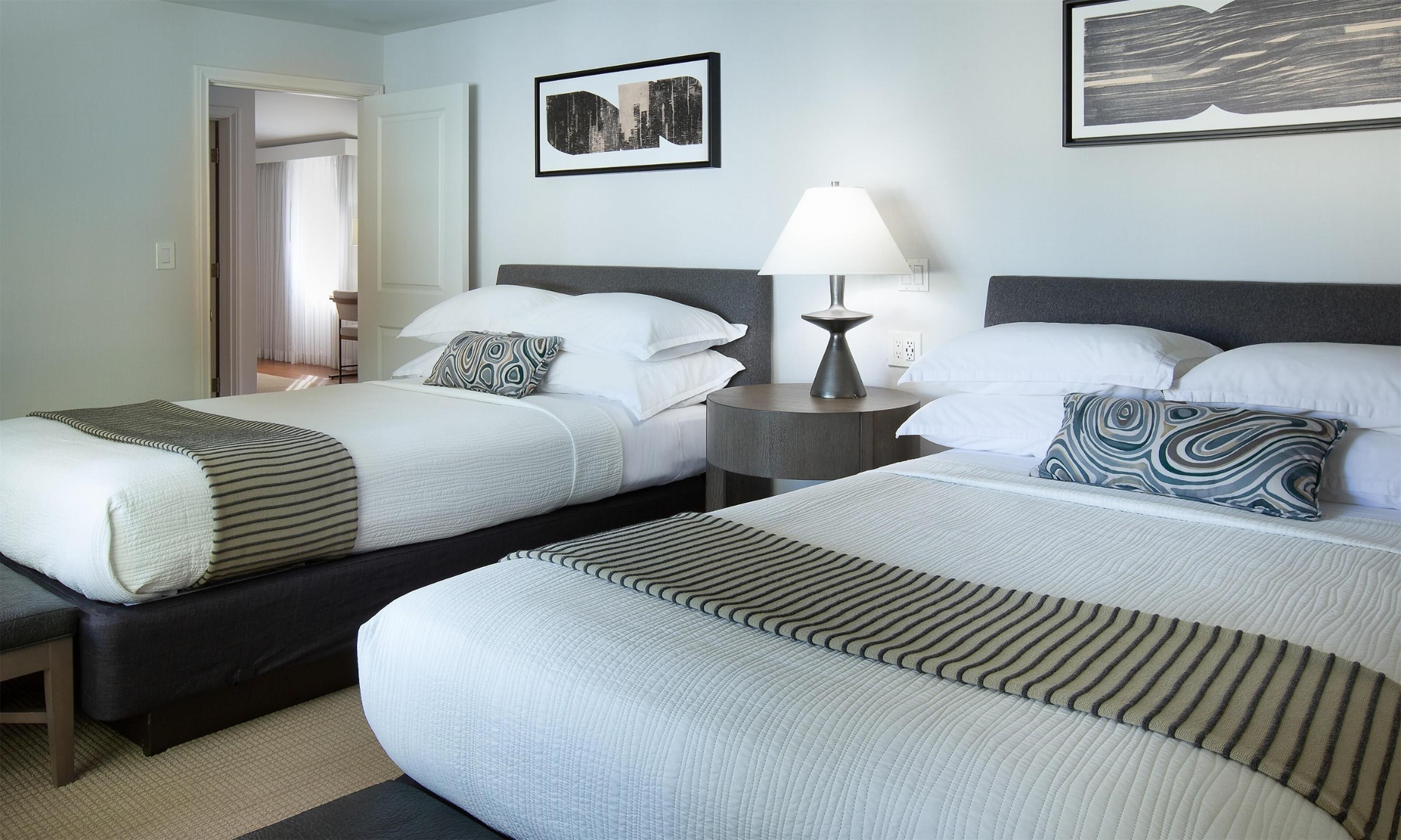 Une chambre d’hôtel avec deux lits, une table de chevet avec une lampe et un tableau encadré au mur.