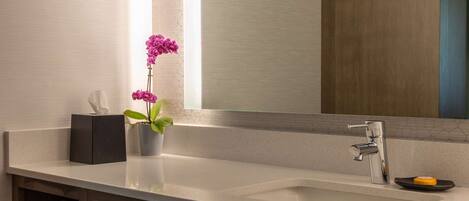 A modern bathroom with a large mirror, a white sink, and a wooden vanity.