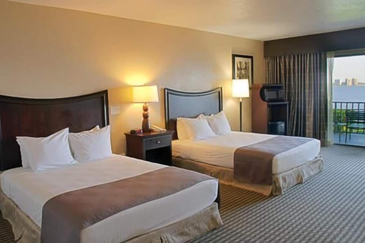 A hotel room with two beds, a television, a lamp, and a view of the city.