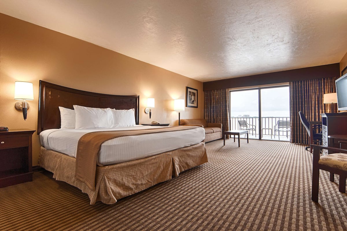 A hotel room with a large bed, a desk, a chair, a TV, and a balcony with a view.