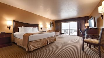 A hotel room with a large bed, a desk, a chair, a TV, and a balcony with a view.