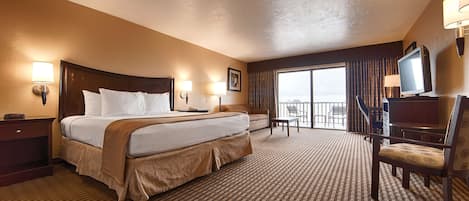 A hotel room with a large bed, a desk, a chair, a TV, and a balcony with a view.