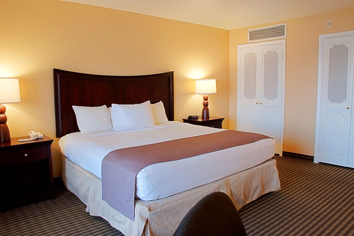 A hotel room with a large bed, two bedside tables, a nightstand, a desk, and a wardrobe.