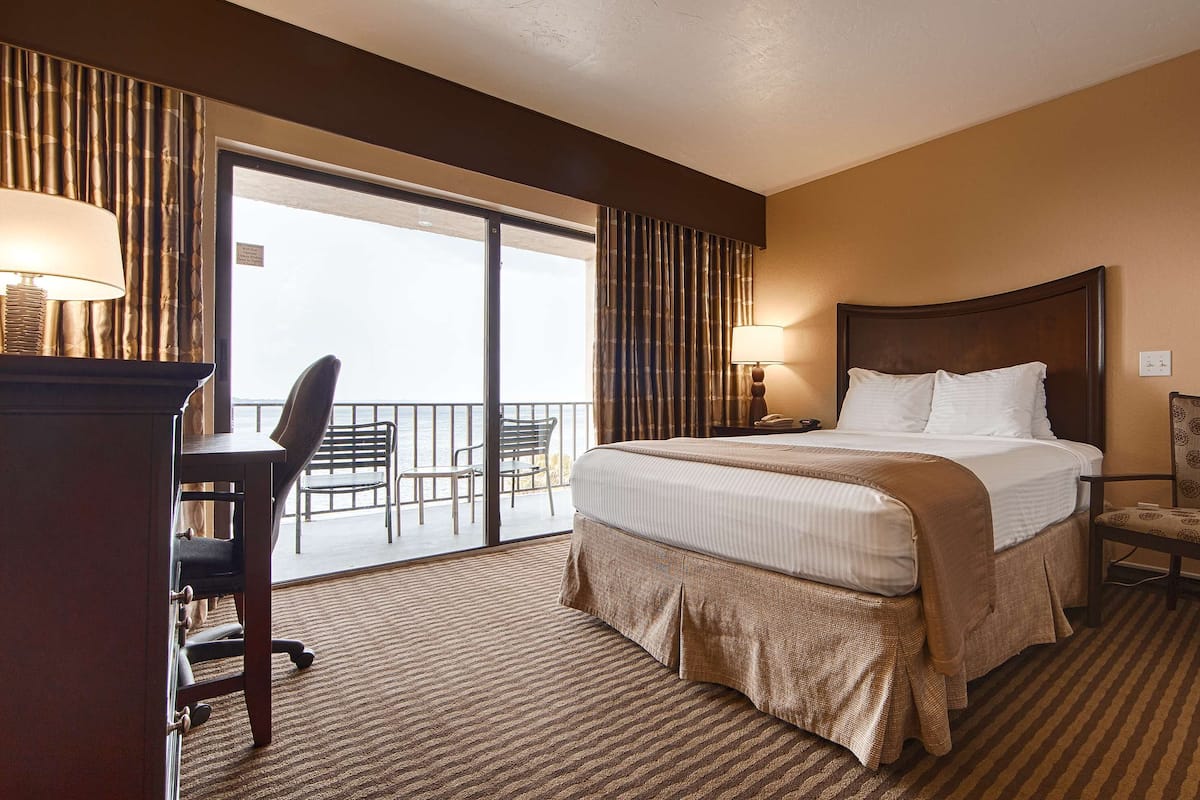 A hotel room with a large bed, a desk, a chair, and a view of the ocean.