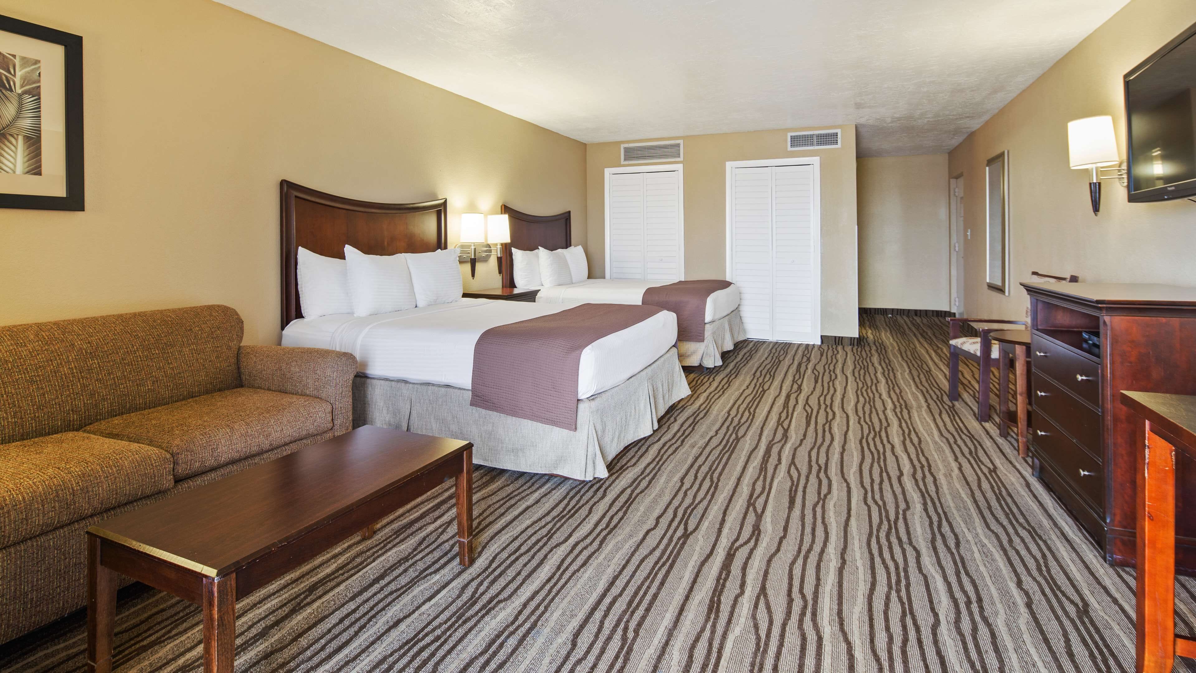 A hotel room with a large bed, two smaller beds, a sofa, a desk, and a dresser.