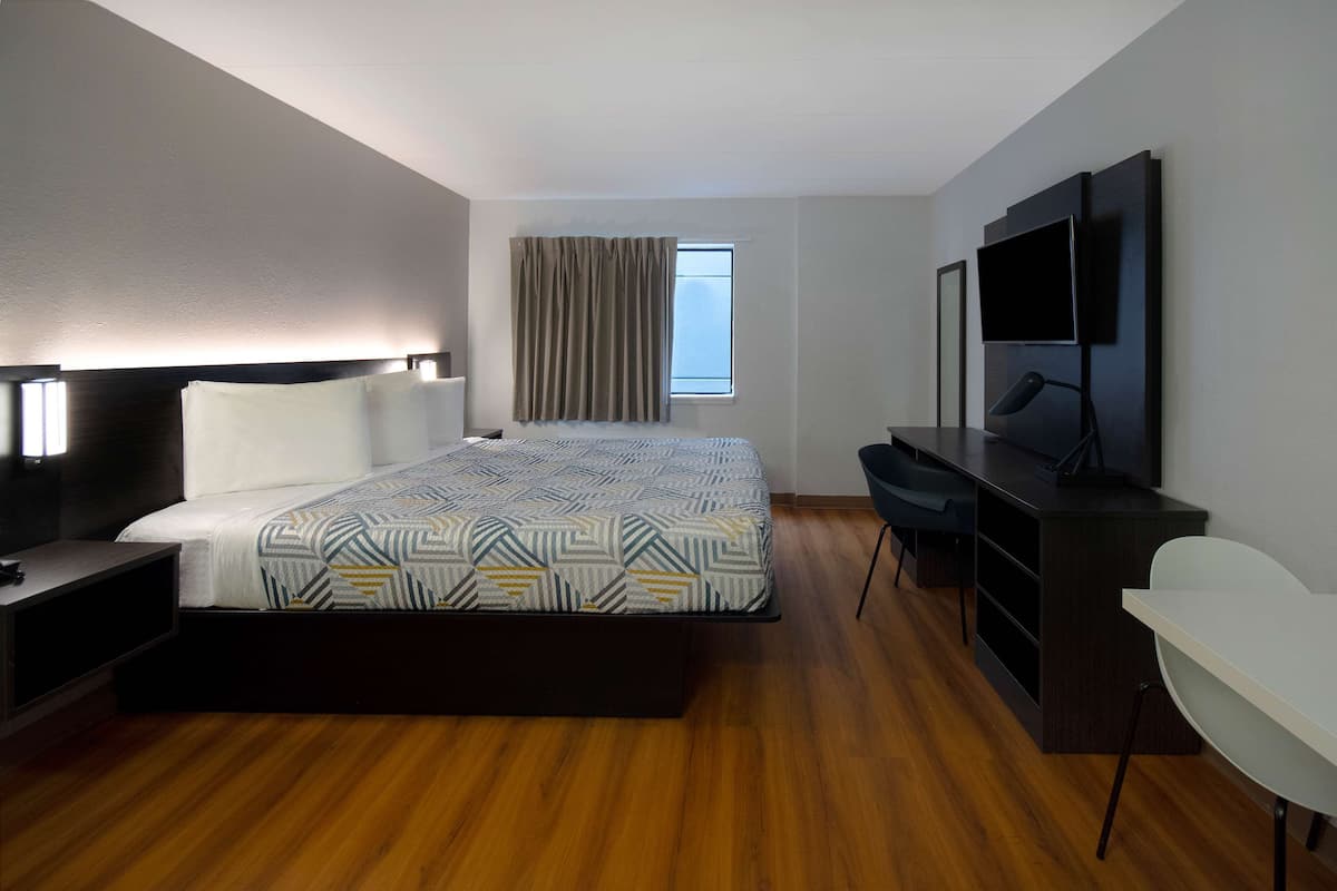 A hotel room with a bed, bedside table, desk, chair, TV, and a window with curtains.
