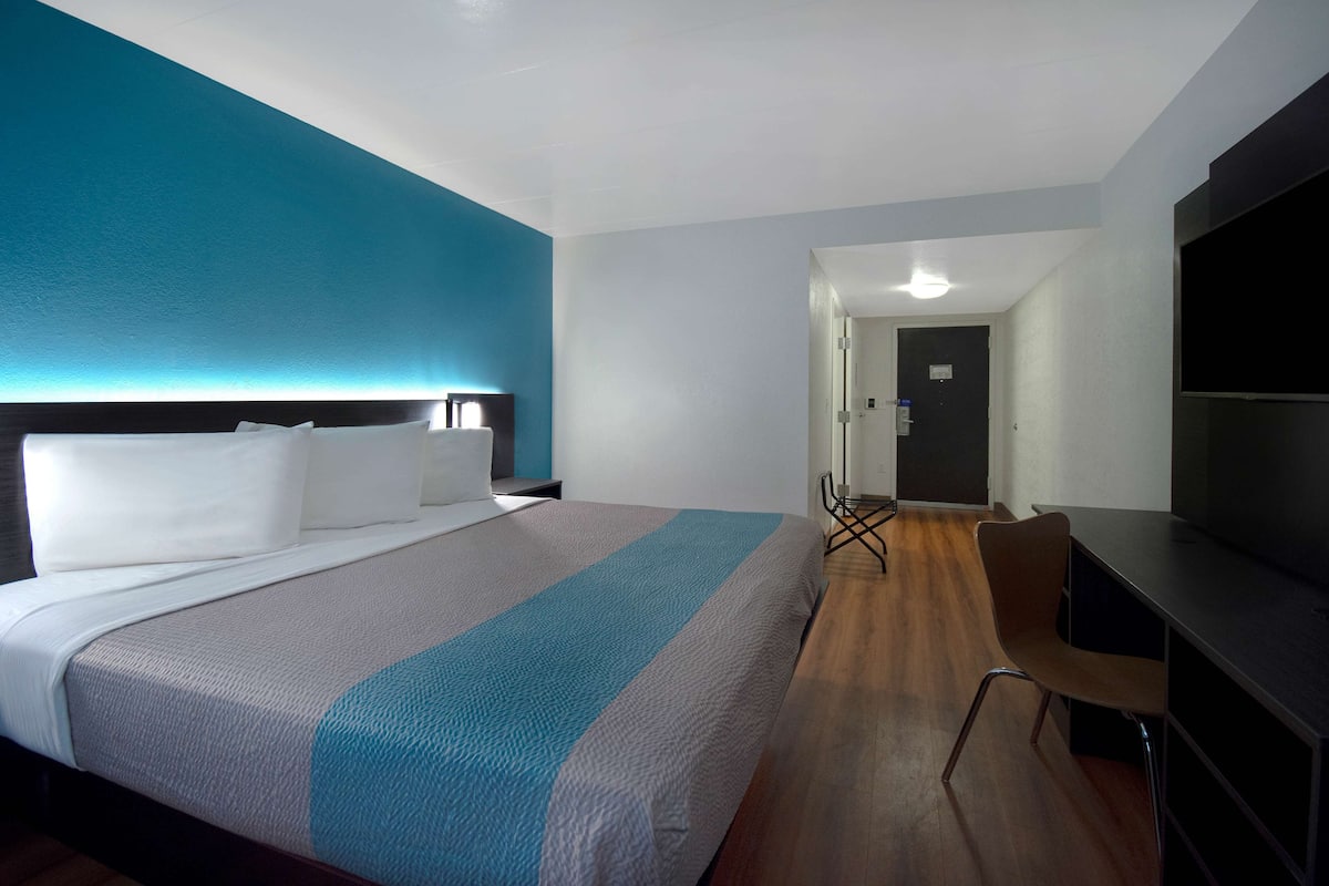 A modern hotel room with a large bed, a desk, and a TV.