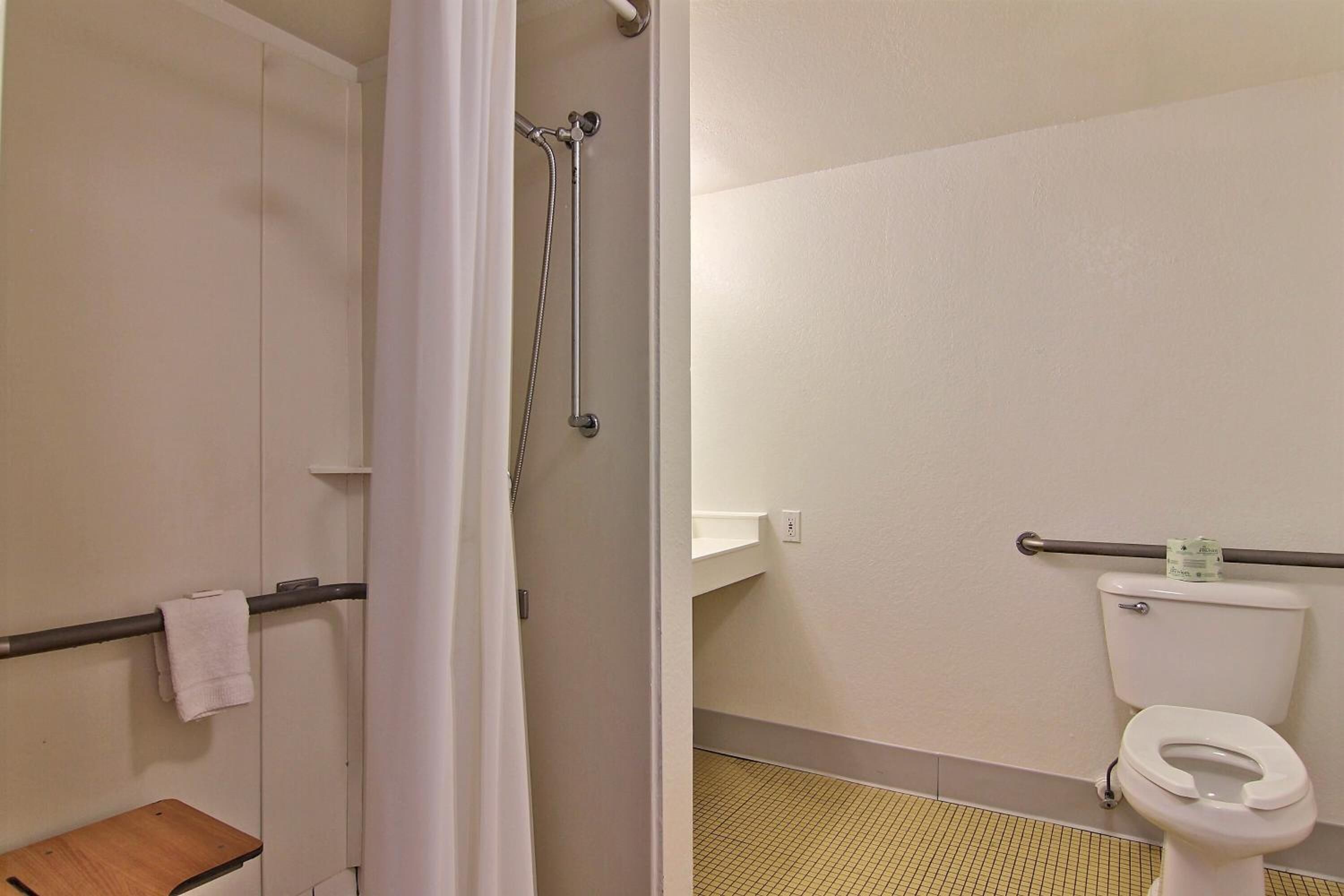 A bathroom with a toilet, grab bar, and shower area.