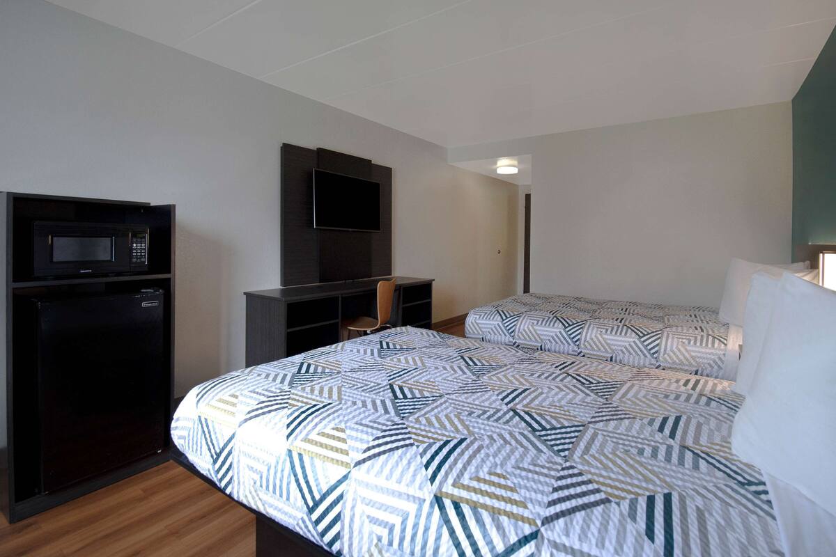 A hotel room with a bed, a desk, a chair, a microwave, and a television.