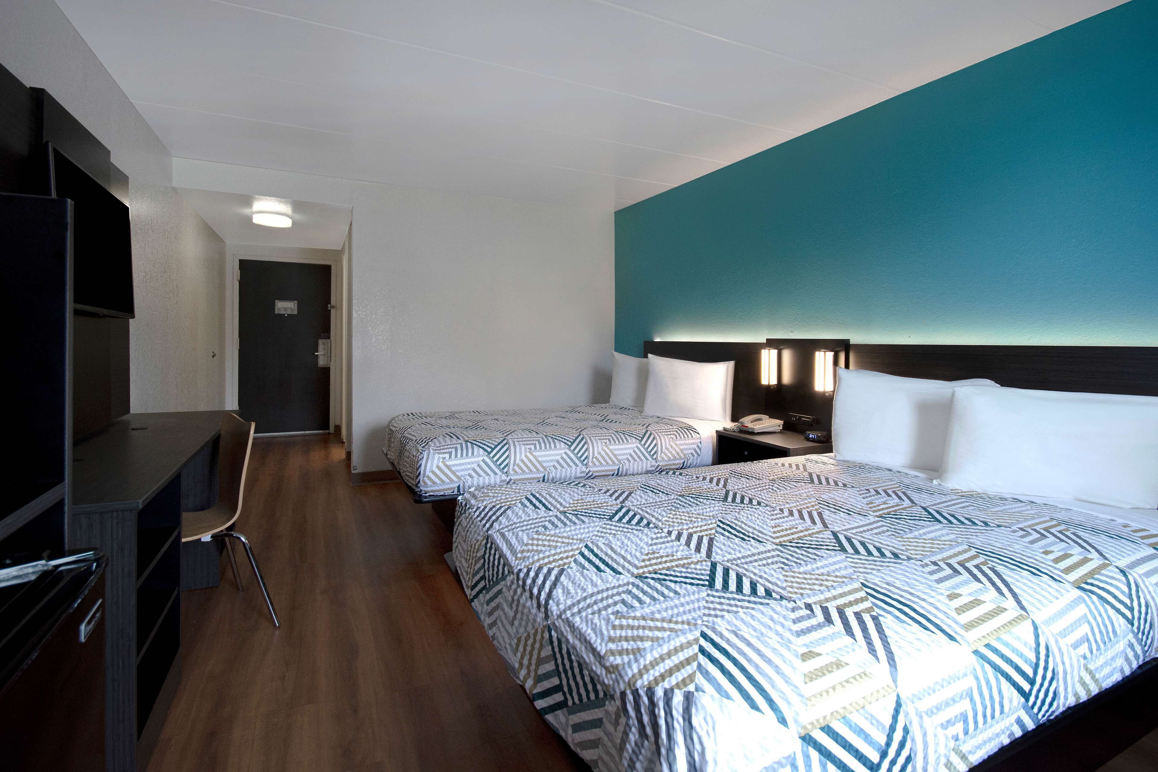 A hotel room with two beds, a desk, and a TV.