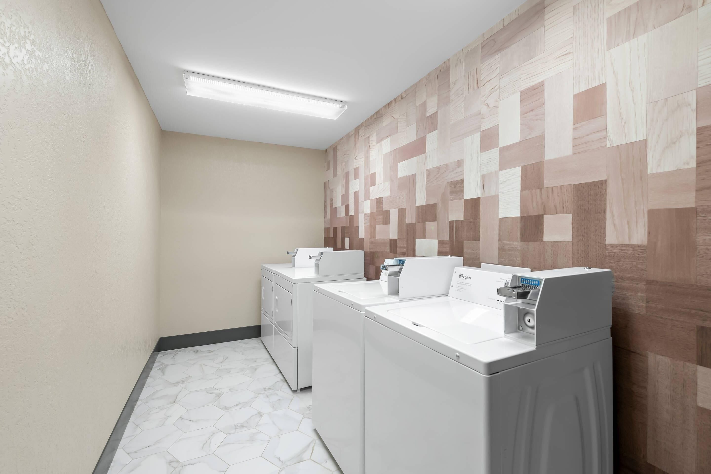 A laundry room with two front-loading washers and dryers, a tiled floor, and a wall with a geometric pattern.