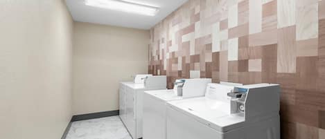 Un lavadero con dos lavadoras y secadoras de carga frontal, suelo de baldosas y una pared con diseño geométrico.