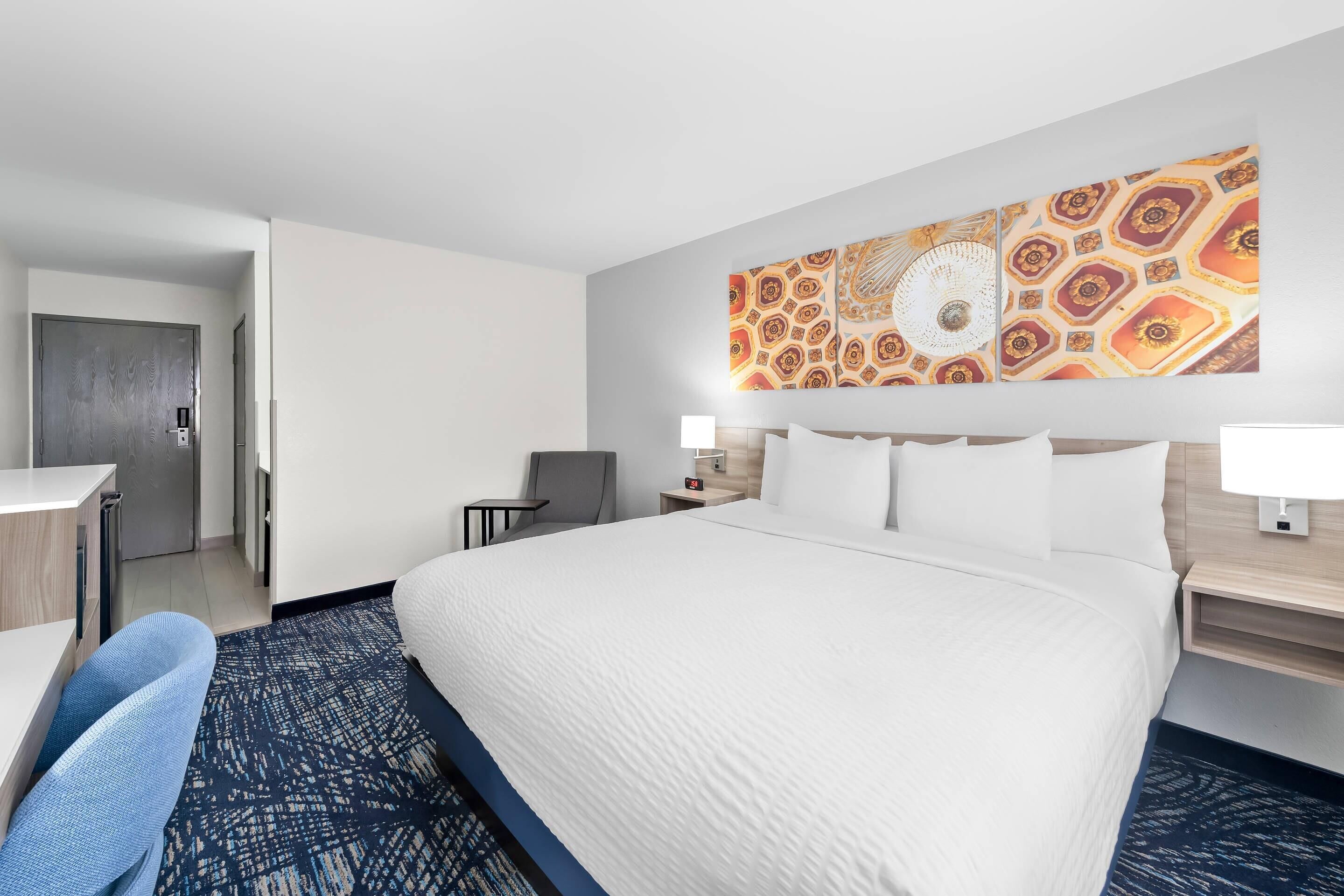 A hotel room with a large bed, a desk, a chair, a nightstand, and a wall art piece.