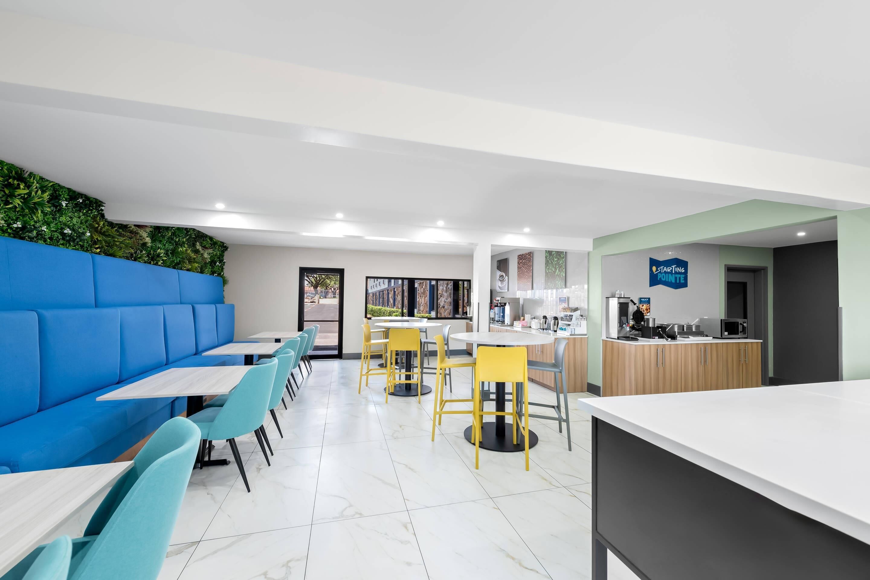 Um restaurante moderno com assentos azuis, cadeiras amarelas e uma área de cozinha.