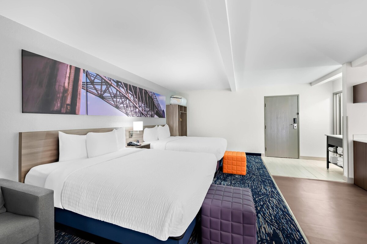 A hotel room with a large bed, two bedside tables, a sofa, a large painting, and a door leading to a bathroom.