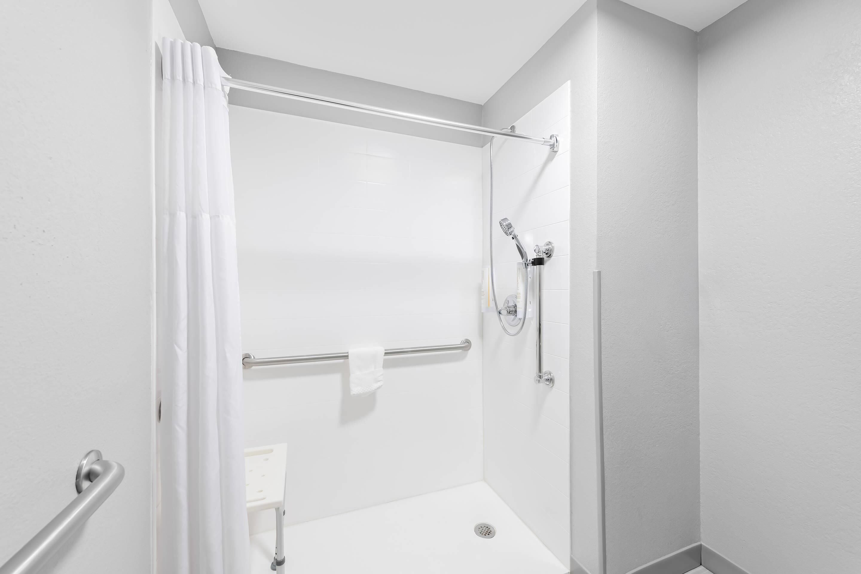 A modern shower area with a glass door, a handrail, and a towel rack.