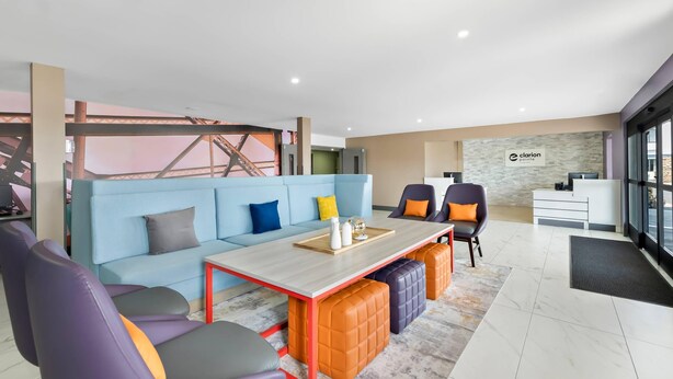 A modern hotel lobby with a blue sofa, purple and orange chairs, a wooden coffee table, and a reception desk.