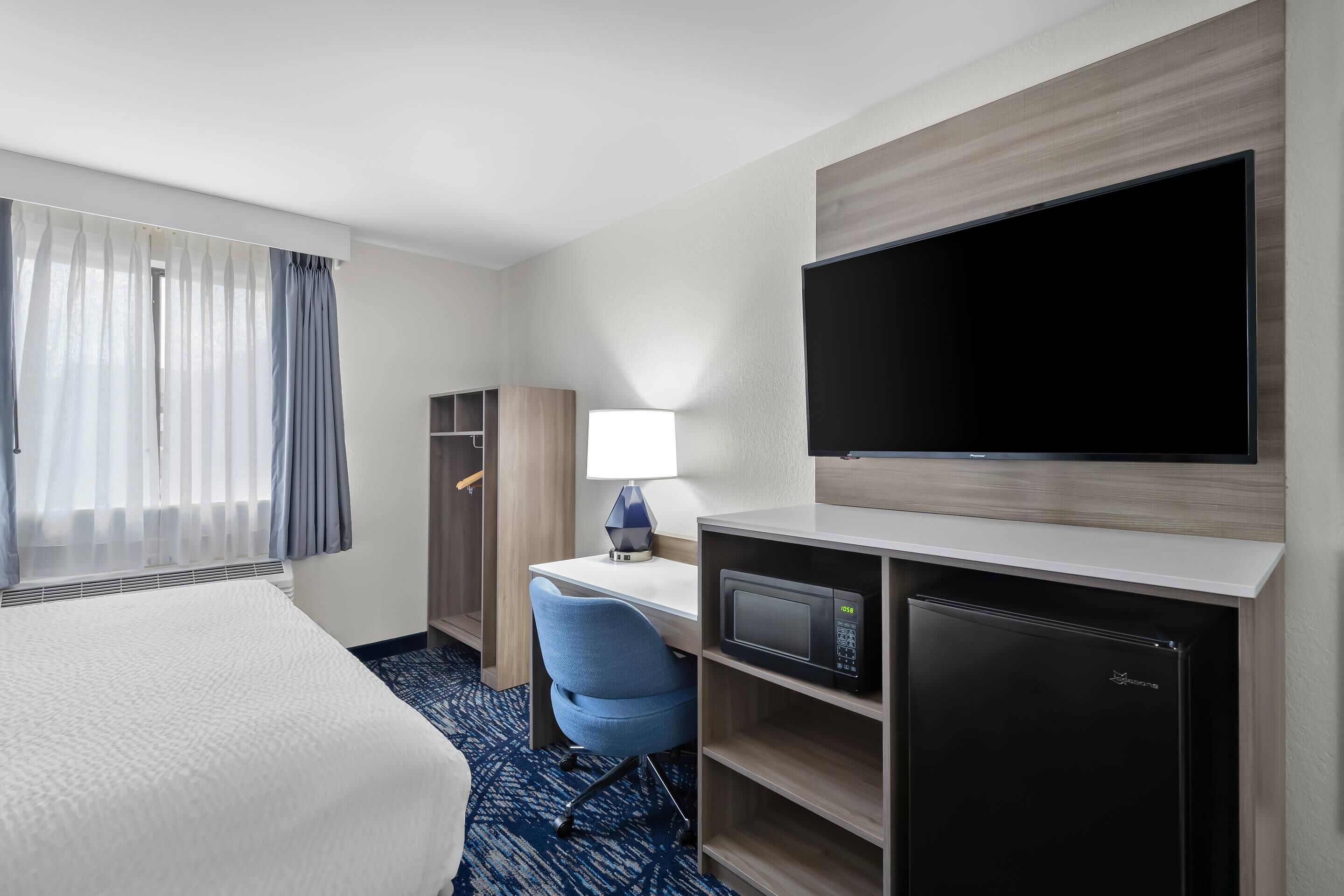 A hotel room with a bed, a desk with a lamp, a TV, a microwave, and a mini-fridge.