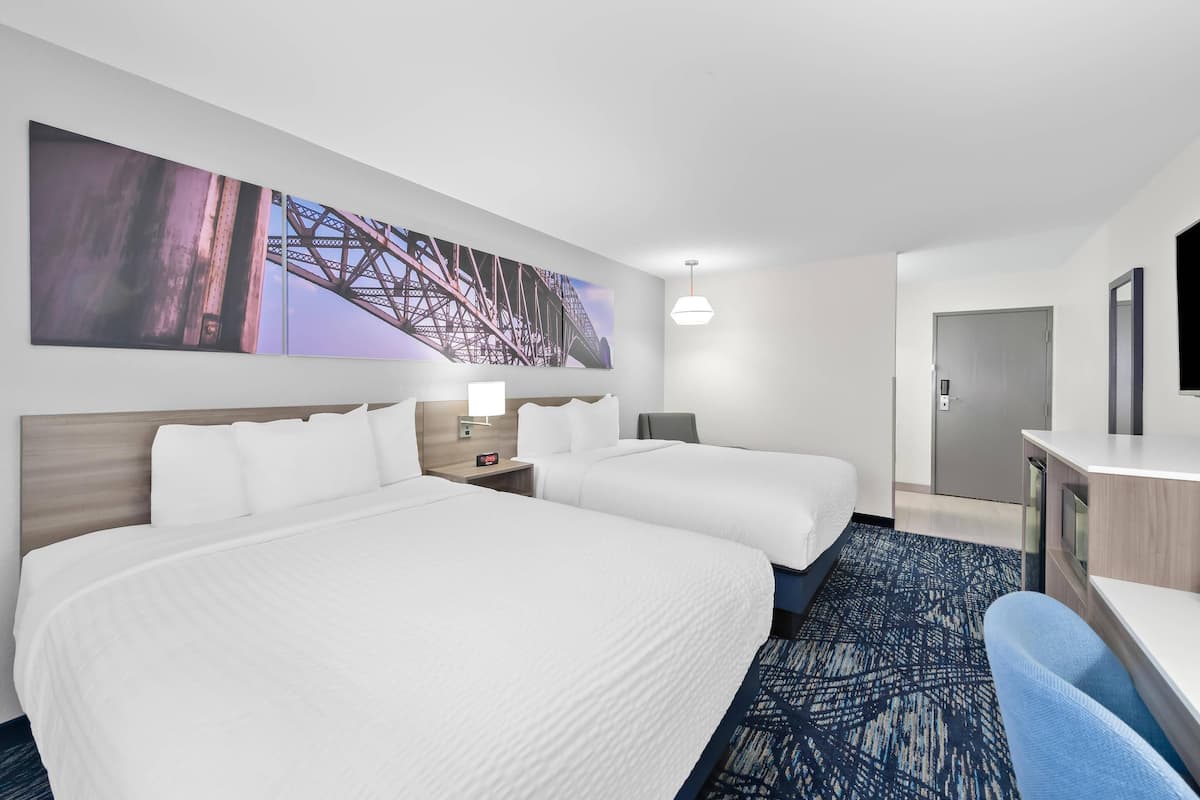 A hotel room with two beds, a desk, a chair, a TV, and a large painting on the wall.
