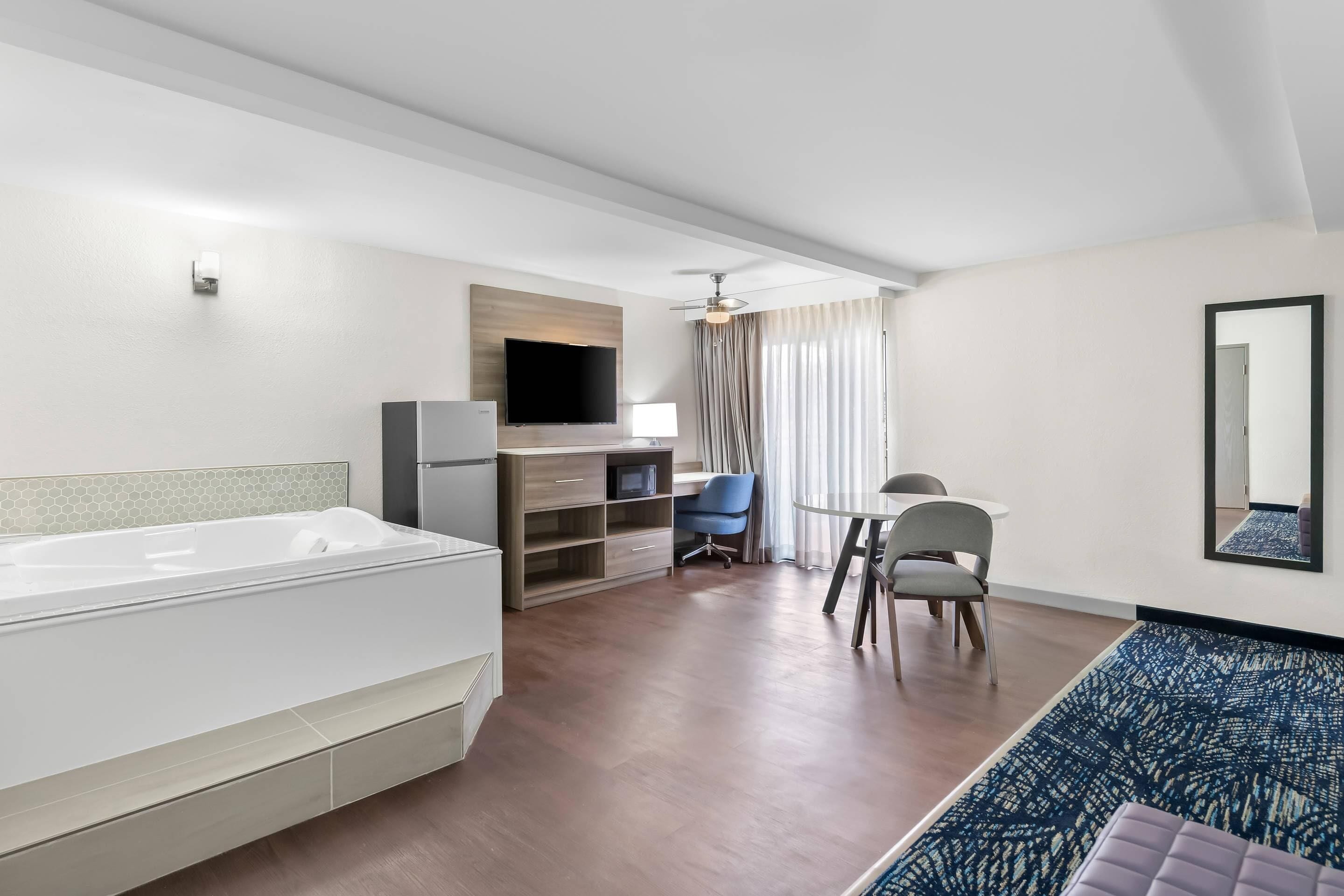 Habitación de hotel moderna con una bañera blanca grande, un escritorio con una silla, un televisor y un ventilador de techo.