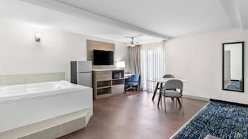 Habitación de hotel moderna con una bañera blanca grande, un escritorio con una silla, un televisor y un ventilador de techo.