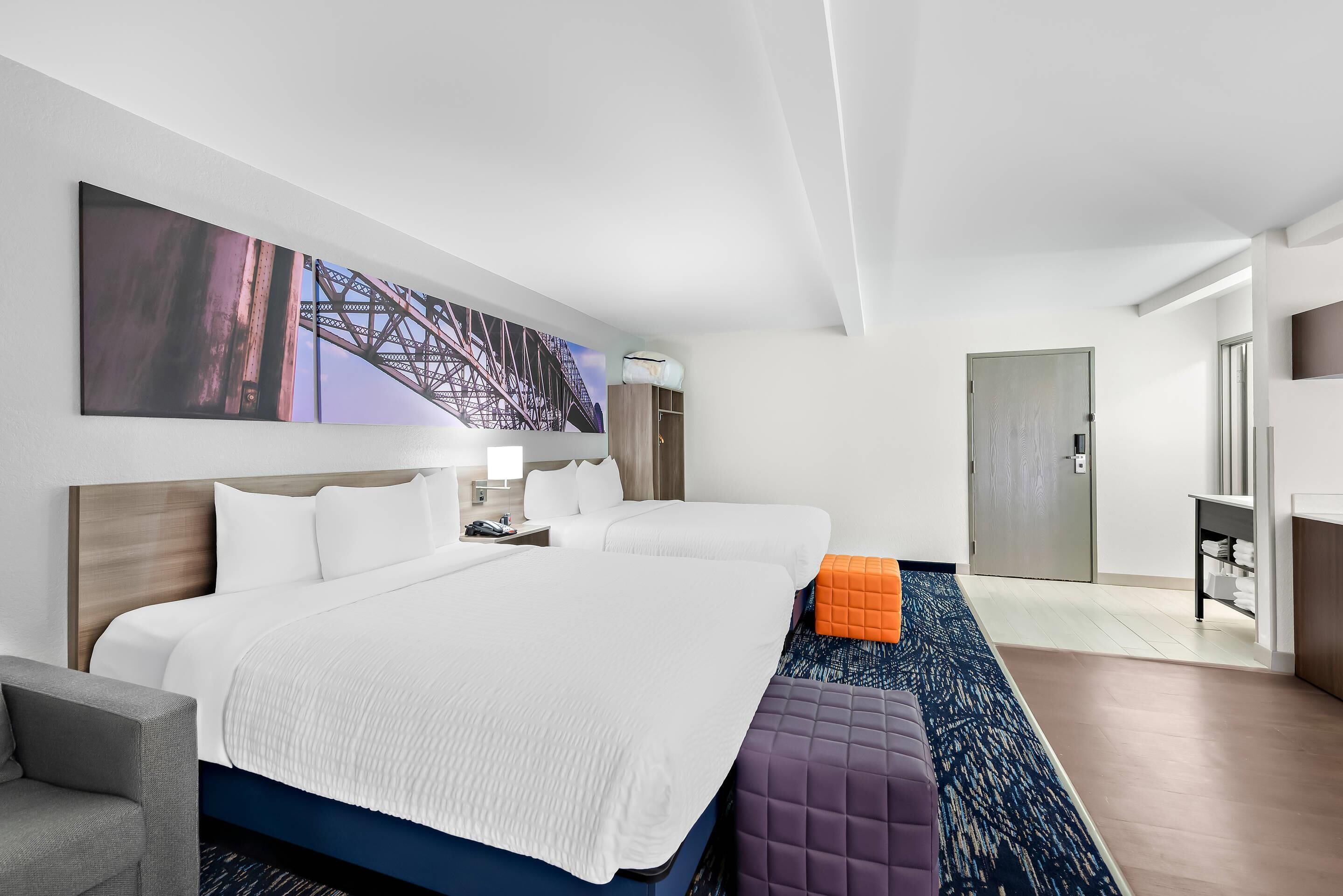 A hotel room with a large bed, two bedside tables, a desk, a chair, and a large window.