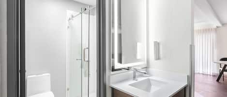 A modern bathroom with a glass shower enclosure, a white toilet, and a vanity with a mirror.