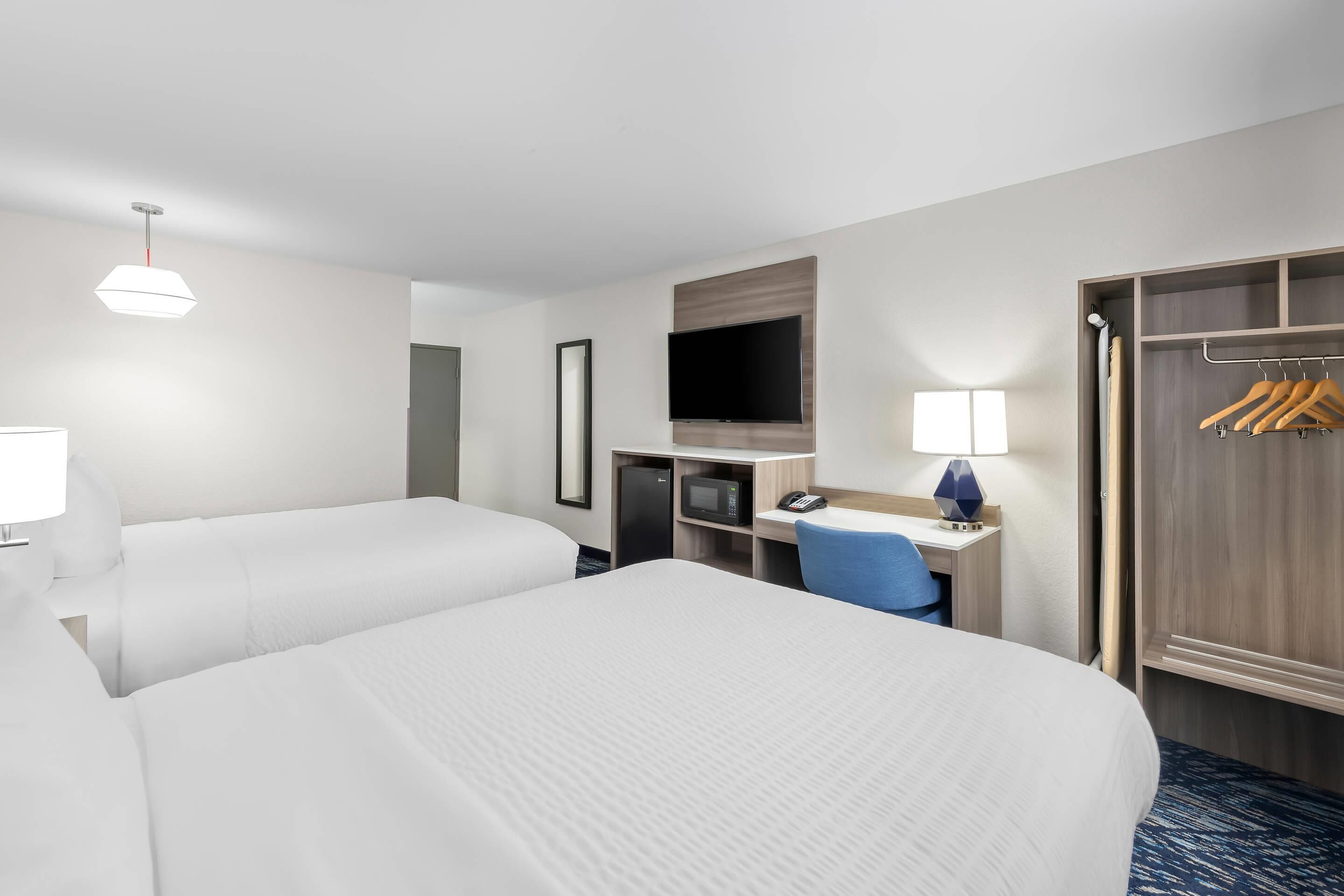 Habitación de hotel con dos camas, un escritorio con computadora, un televisor y un armario.