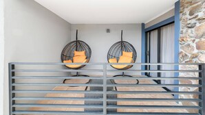 A balcony with two hanging chairs, a stone wall, and a view of the interior.