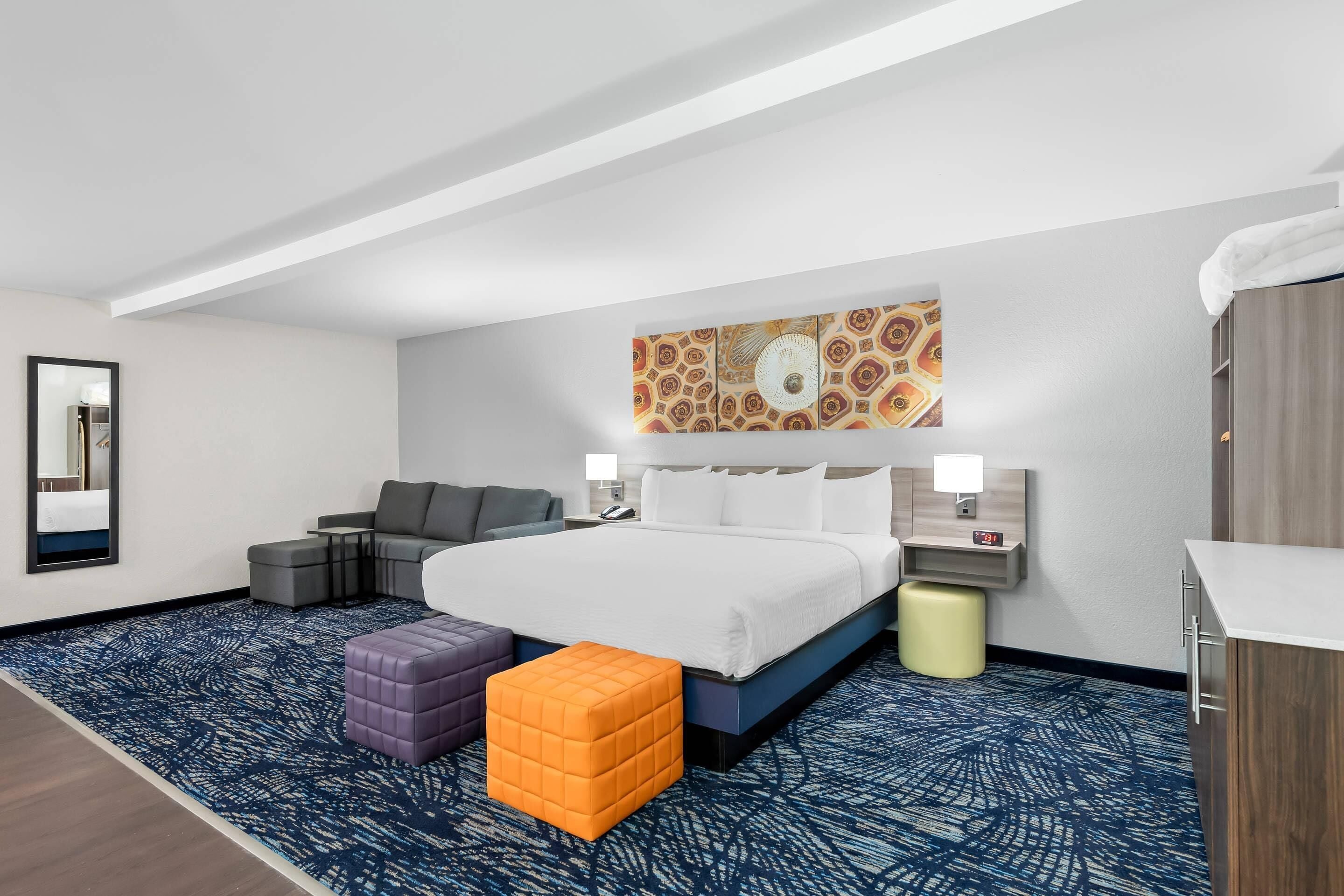 A hotel room with a large bed, a sofa, a small table, and a decorative wall piece.