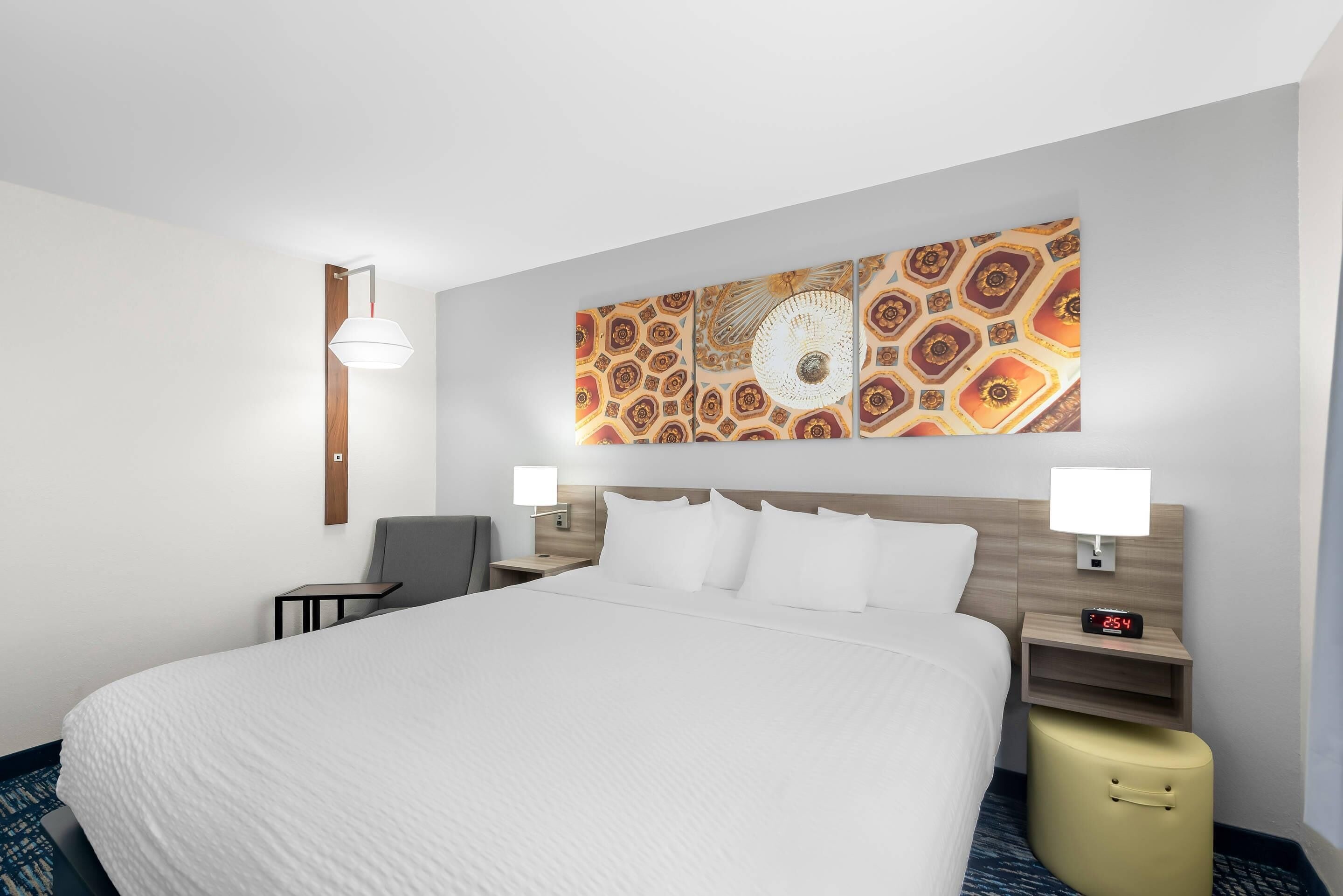 A hotel room with a large bed, two bedside tables with lamps, a wall-mounted clock, and a decorative wall piece.