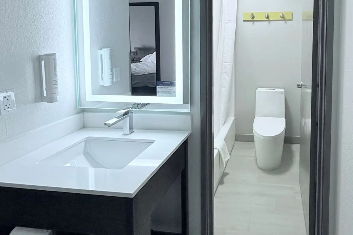 A modern bathroom with a large mirror, a sink, and a toilet.
