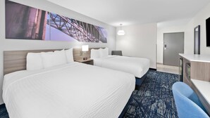 A hotel room with two beds, a desk, a chair, a large painting on the wall, and a door.