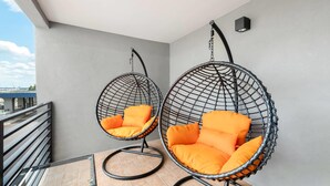 Two hanging chairs with orange cushions on a balcony with a tiled floor and a railing.