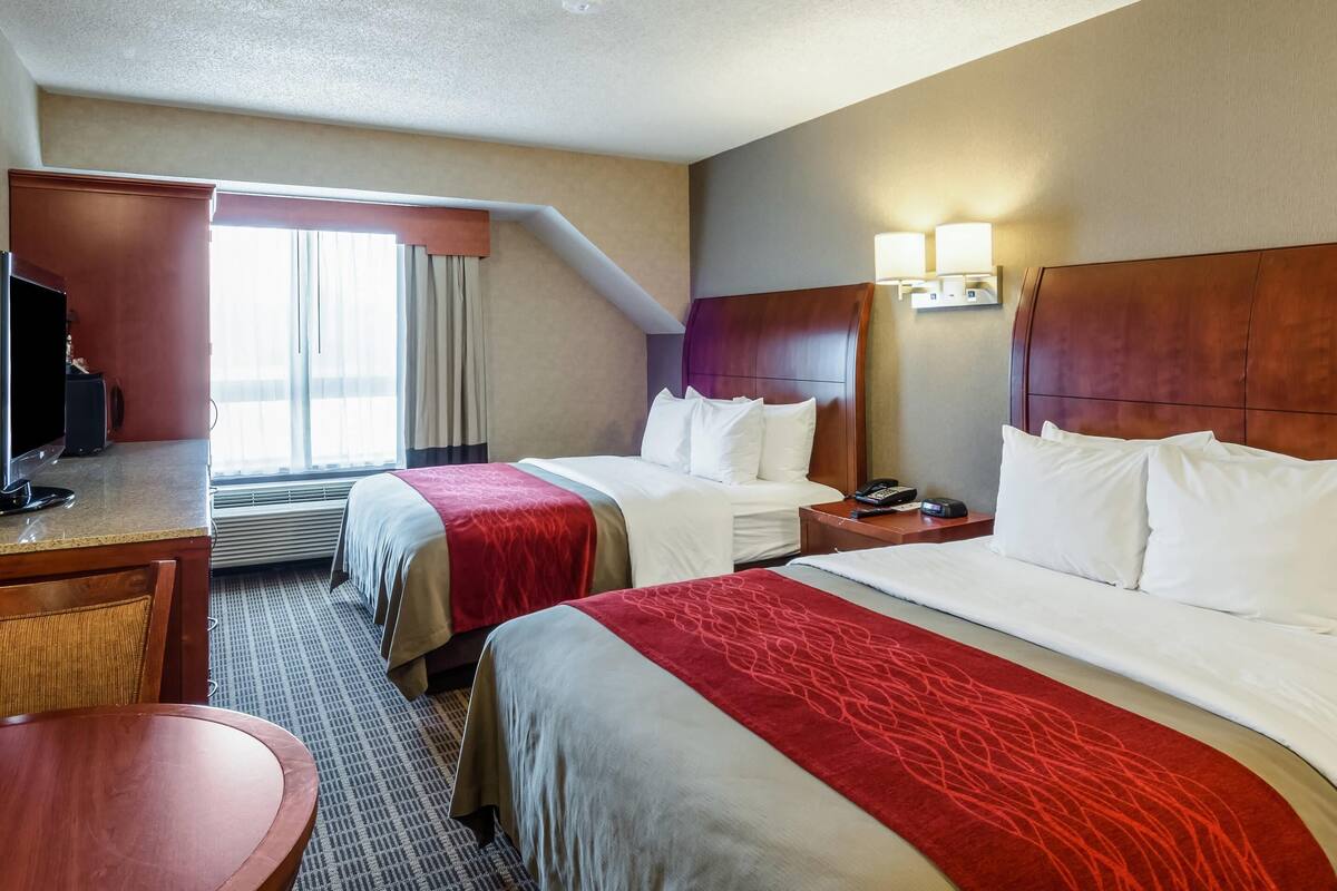 Quarto de hotel com duas camas, uma escrivaninha, televisão e janela com cortinas.