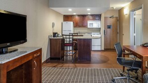A compact hotel room with a kitchenette, a flat-screen TV, a dining area with a table and chairs, and a patterned rug. - Comfort Inn & Suites West Springfield (West Springfield)