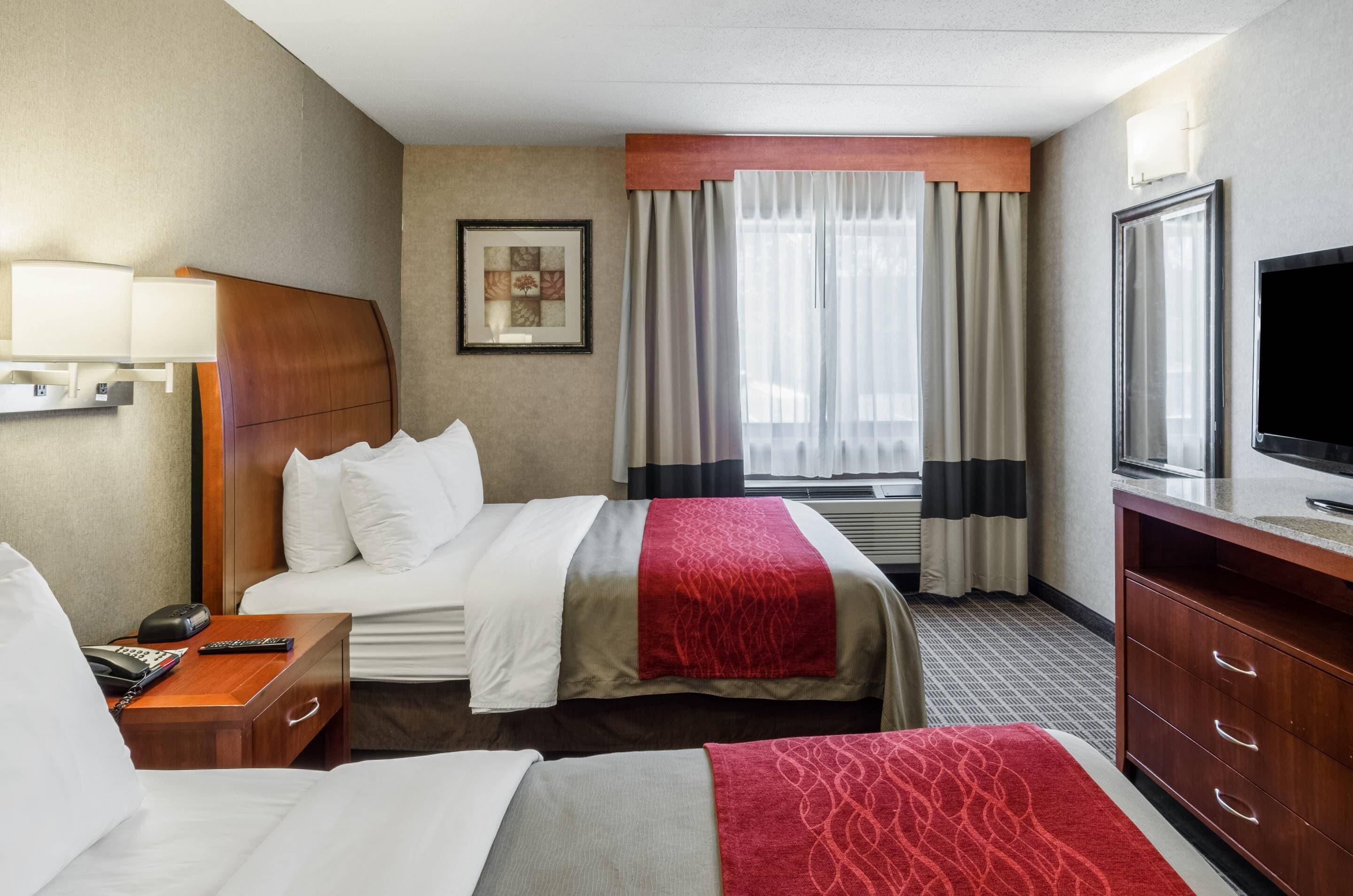 A hotel room with two beds, a TV, a desk with a lamp, and a window with curtains.