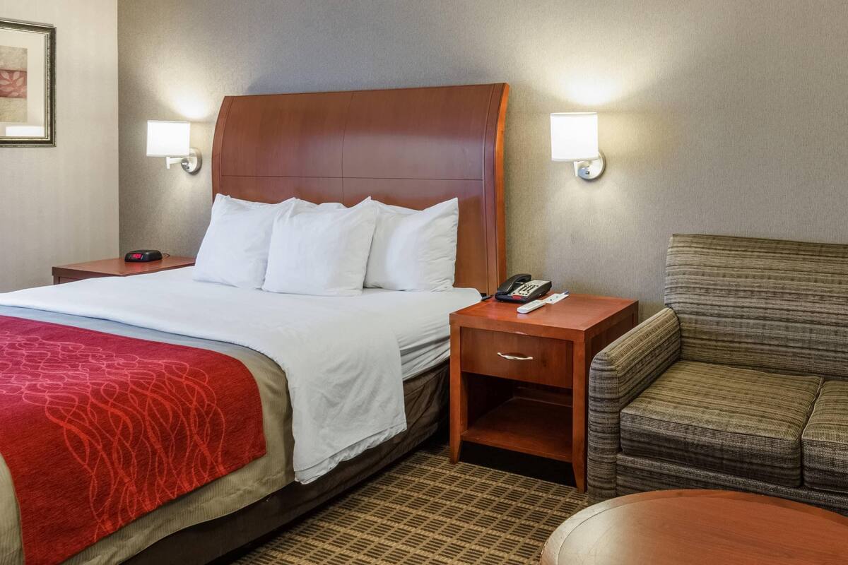 Quarto de hotel com uma cama grande, duas mesas de cabeceira, uma cadeira e uma pequena mesa.
