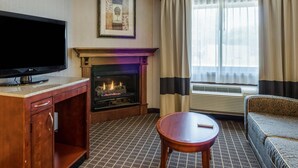 A hotel room with a flat-screen TV, a fireplace, a sofa, a small table, and a window with curtains. - Comfort Inn & Suites West Springfield (West Springfield)