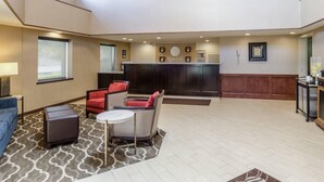 A hotel lobby with a reception desk, seating area with chairs and ottoman, and a patterned rug on the floor. - Comfort Inn & Suites West Springfield (West Springfield)