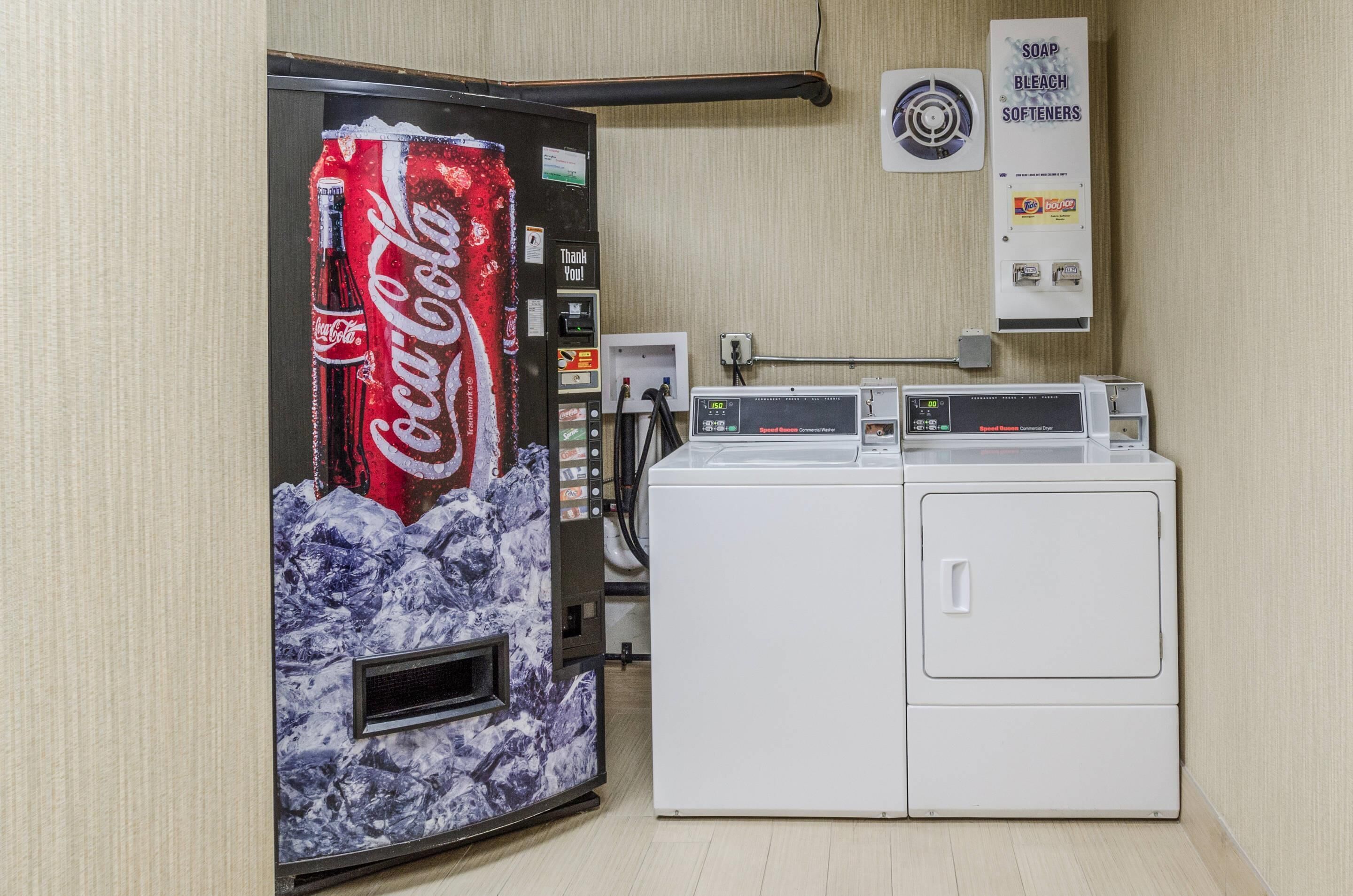 Une laverie équipée d’un distributeur automatique de Coca-Cola, d’un sèche-linge et d’un distributeur de savon mural.